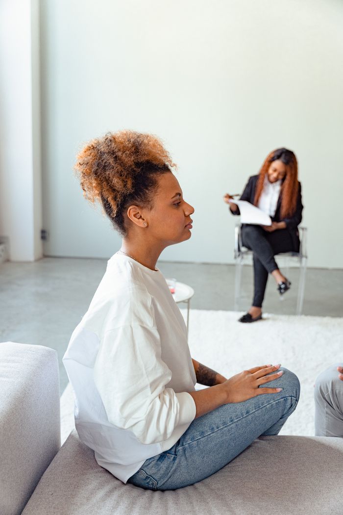 A woman in a psychotherapy session sitting on a couch, with a therapist taking notes.
